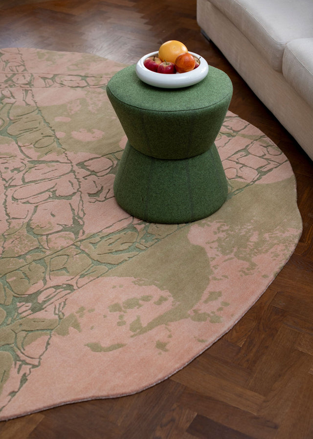 Green stool on a pink and green patterned rug with fruit bowl on top