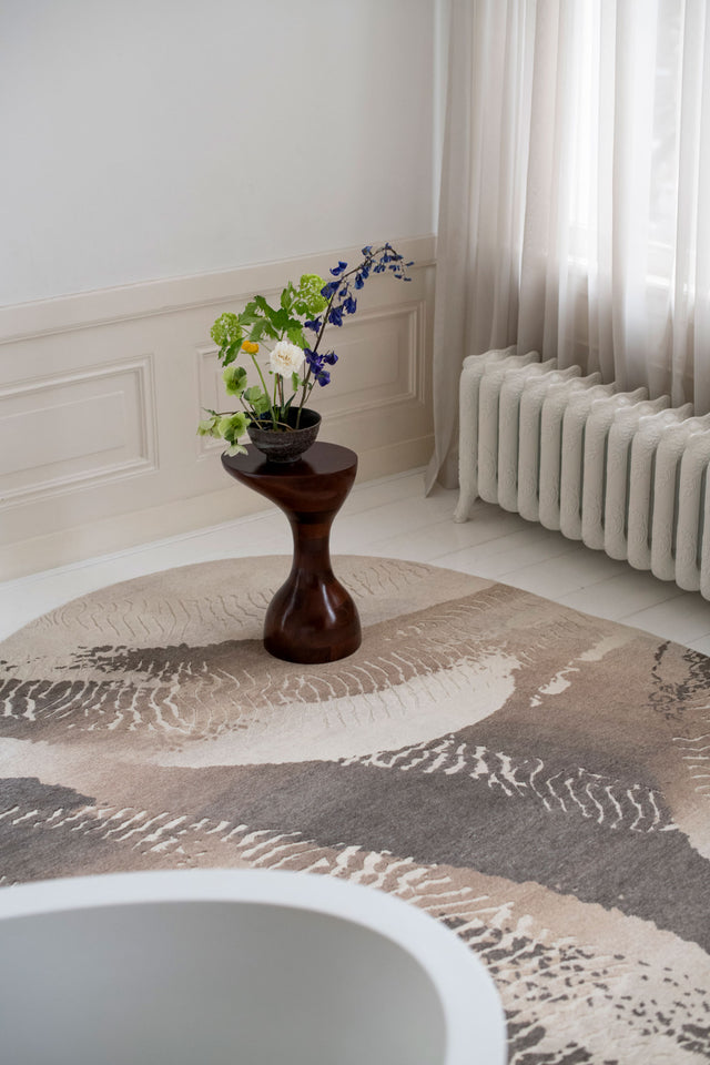 Decorative rug with a pattern, wooden side table with flowers, and radiator in a room.
